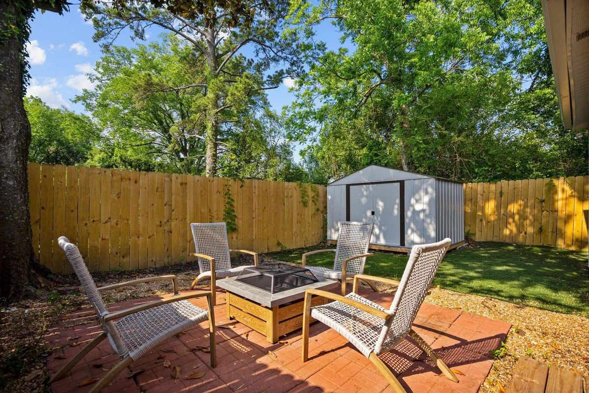 This image showcases a cozy backyard patio featuring a fire pit surrounded by inviting seating, with a garden shed and lush greenery setting a private and welcoming backdrop. The atmosphere suggests a perfect setting for evening gatherings or relaxation in the fresh air.