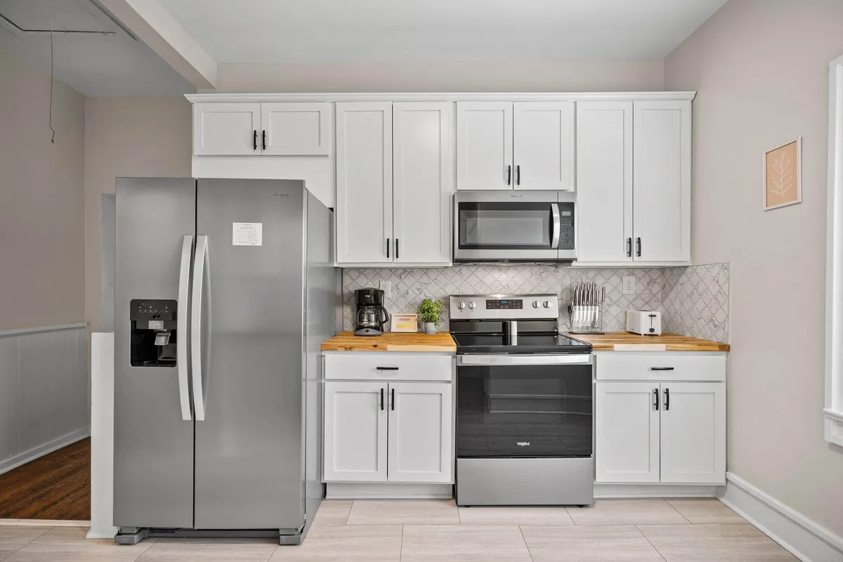 A fresh, contemporary kitchen scene featuring a stainless steel refrigerator, black stove, wooden countertop, and white cabinets. The arrangement suggests a space ideal for both everyday meal preparation and hosting family feasts.