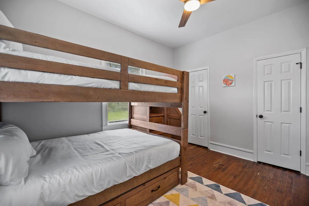 This interior view shows a second bedroom with a full-over-full bunk bed, a colorful rug, wooden flooring, and playful artwork on the wall. The inviting setup is ideal for children or guests, with ample sleeping space and a sense of family-friendly comfort.