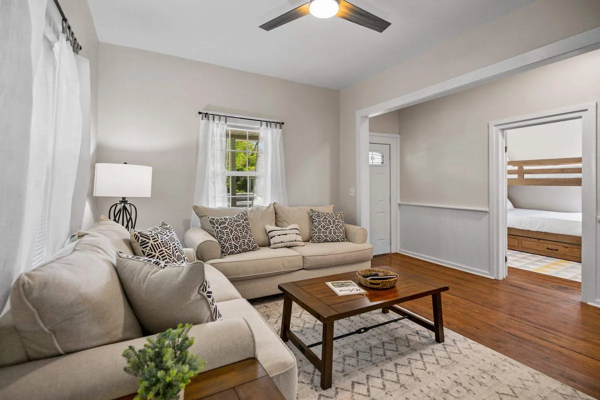 This cozy living room scene includes a sofa, coffee table, lamp, and window. The inviting arrangement is perfect for unwinding, reading, or socializing, while the sofa subtly hints at its functionality as a pullout bed for extra sleeping space.