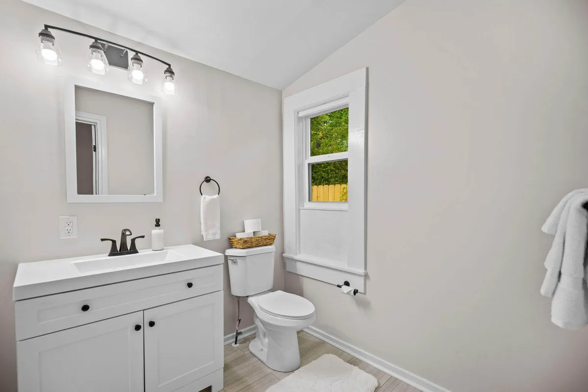 A stylish, inviting vanity area with a sink and large mirror, softly lit by a nearby window. The space emanates tranquility, offering a peaceful setting for morning routines or personal moments.